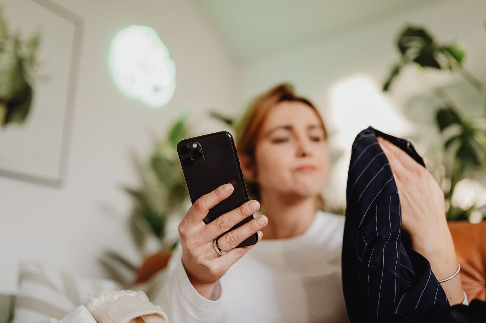 Vrouw bekijkt een kledingstuk en zoekt op haar telefoon naar een kortingscode