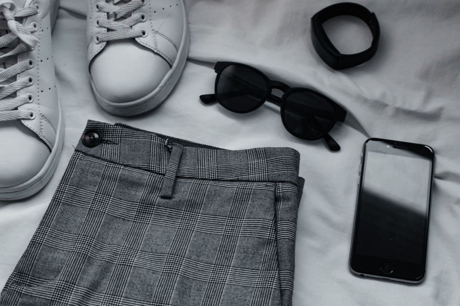 Sneakers, zonnebril, broek en telefoon naast elkaar op een lichte ondergrond